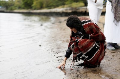Indigenous woman touches water. © Credit – REUTERS