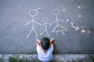 Overhead shot of little boy drawing a picture of his family and feeling sad. © Getty Images
