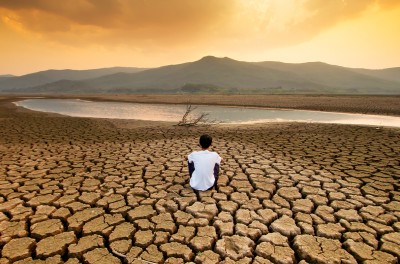 A child sitting on a drying lake underneath an orange-coloured polluted sky. ISTOCK / GETTY IMAGES PLUS