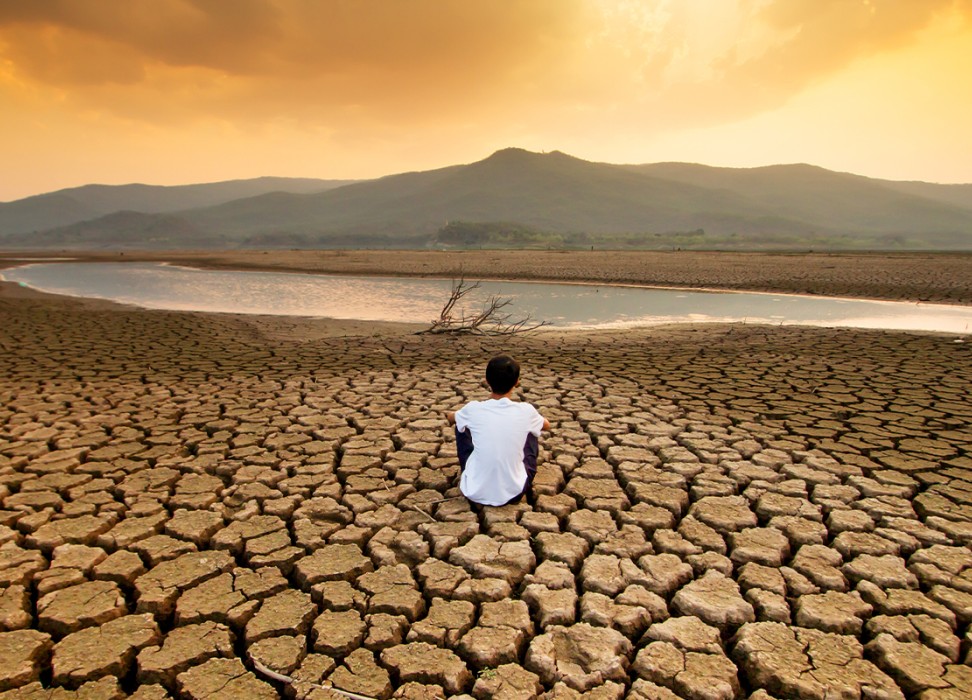 A child sitting on a drying lake underneath an orange-coloured polluted sky. ISTOCK / GETTY IMAGES PLUS