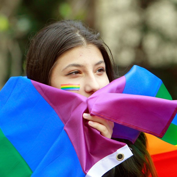 A member of Romania's LGBTQ (Lesbian, Gay, Bisexual, Transgender and Queer) community carries a rainbow-colored flag and the European Union (EU) flag in downtown Bucharest, Romania,