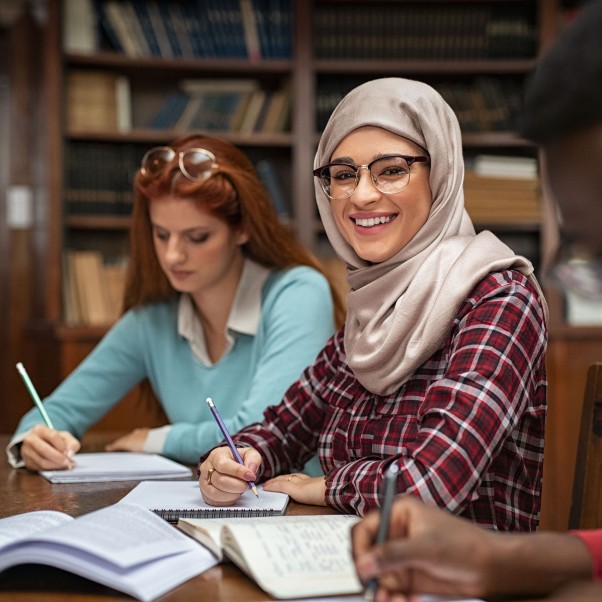 Portrait of smiling female student wearing abaya studying with multiethnic students. © Getty Images