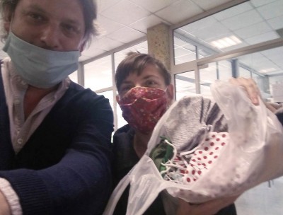 Two people in protective face masks hold up a bag of handmade masks intended for people who are homeless and social workers.