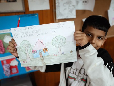 A young child from the Crvena Zvezda settlement shows a drawing he made, which features the Indigo community center, Serbia. © Stefan Vidojević from MaxNova Creative