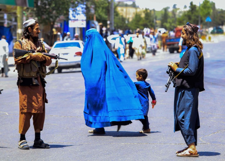 Afghan woman and child walking past Taliban soldiers © Credit – EPA-EFE