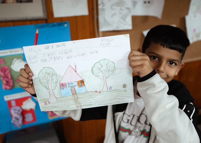 A young child from the Crvena Zvezda settlement shows a drawing he made, which features the Indigo community center, Serbia. © Stefan Vidojević from MaxNova Creative