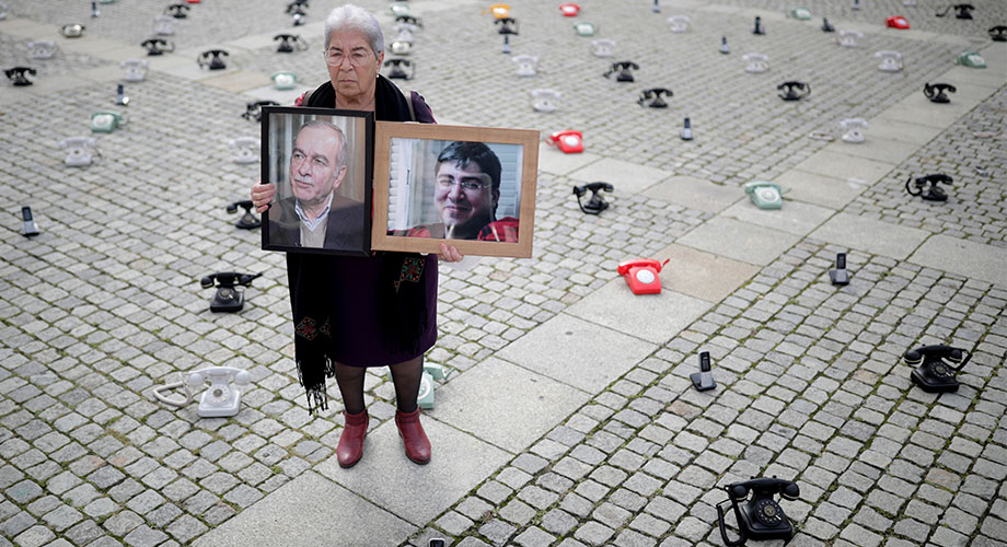 Fadwa Mahmoud sujeta los retratos de su hijo y su marido,  desaparecidos en 2012, al mismo tiempo que unos 300 teléfonos fijos colocados  por familias sirias se encuentran en la Bebelplatz de Berlín (Alemania) como  llamamiento a los gobiernos para que pongan más empeño en buscar información  sobre las personas detenidas en Siria, 28 de agosto de  2021&nbsp;REUTERS/Hannibal Hanschke