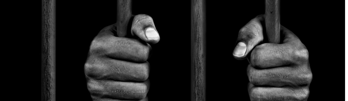 Gros plan sur les mains d’un détenu se tenant à des barreaux. © Getty Images
