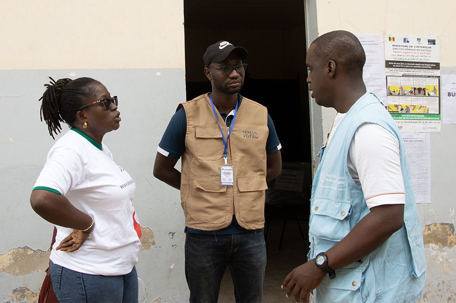 Jaly Badiane (left) of the Senegal Vote initiative and Mouhamadou Sow (right) from OHCHR WARO talk to Emmanuel Baloucoune (middle), a volunteer in charge of election observation at the Demba Diop polling centre. © OHCHR WARO - Habibou Dia