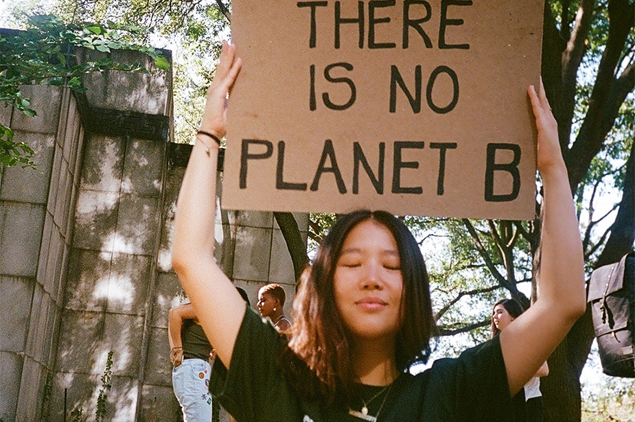 A woman of Asian descent, wearing a black t-shirt, holding a placard that says ‘There is no planet B’
