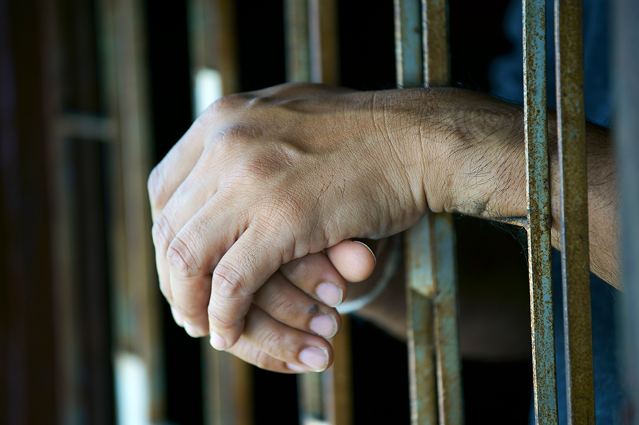 The hands of a person rest between prison bars. © Getty Images/sakhorn38