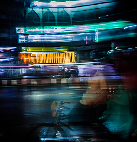 A rickshaw puller waits for passengers, on a rainy night on wet street. Photo by Syed Foyez Uddin on Unsplash (@genetx)