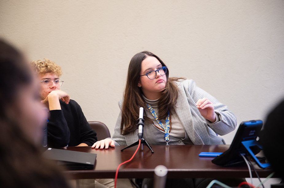 Anghelina (right) and Fran (left) sitting at a table with a microphone, December 2023, Geneva, Switzerland. © OHCHR/Irina Popa