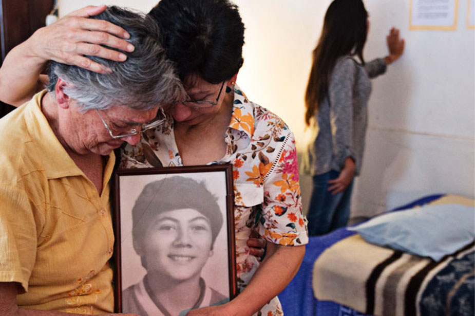 Two women mourn their disappeared family member by hugging their photo.