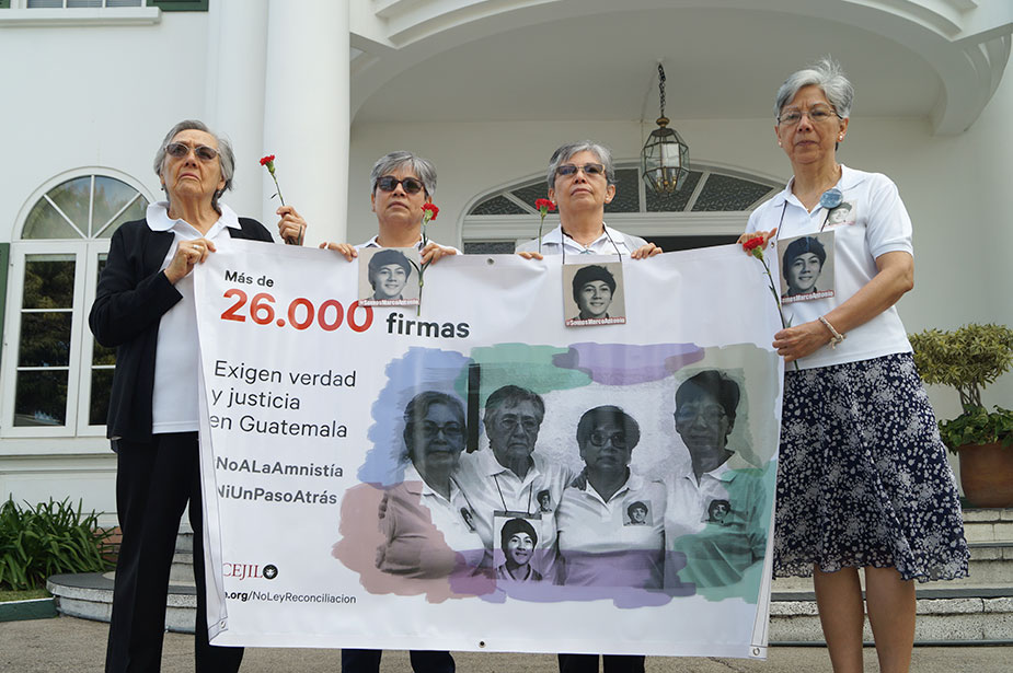 A group of female activists hold a large banner and red flowers in their hands.    