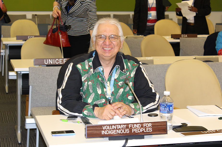 A white haired man sitting down smiles to the camera