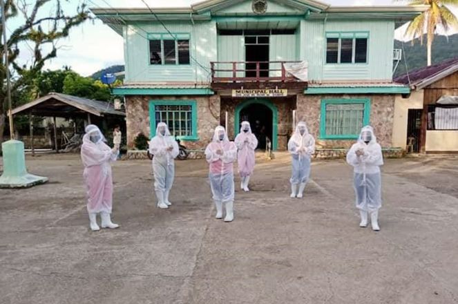 Health workers in full PPE stand outside a municipal hall.