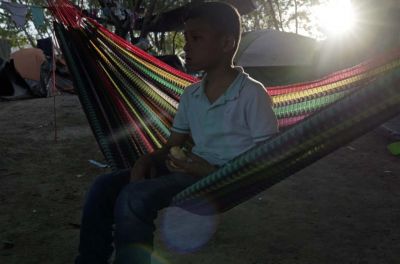 A boy sits in a hammock. Tents are in the background.