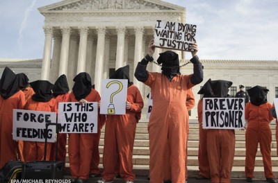 抗议者们身穿橙色的连体衣，站在建筑物前手持标语牌。