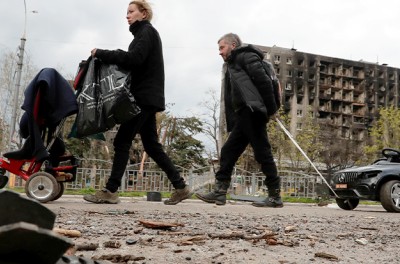 2022年4月22日，在乌克兰南部港口城市马里乌波尔，家庭成员走在俄乌冲突中被损毁的住宅楼附近的街道上。