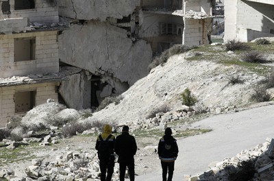 Plusieurs personnes marchent devant des bâtiments détruits à Jabal al-Arbaeen, tenu par les rebelles, dans la province d’Edleb, au sud de la Syrie, le 20 mars 2022. © Reuters