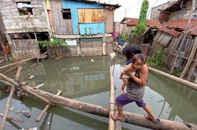 A villager holding a baby maneuvers on a makeshift bridge at a flooded community brought by Typhoon Conson in Muntinlupa city, Metro Manila, Philippines, 10 September 2021 © Francis R. Malasig/EPA-EFE