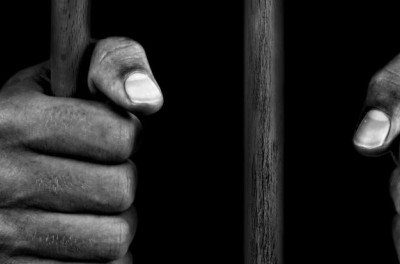 Gros plan sur les mains d’un détenu se tenant à des barreaux. © Getty Images