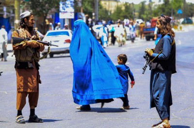 Una mujer y un niño afganos pasan caminando por delante de soldados talibanes © Credit – EPA-EFE