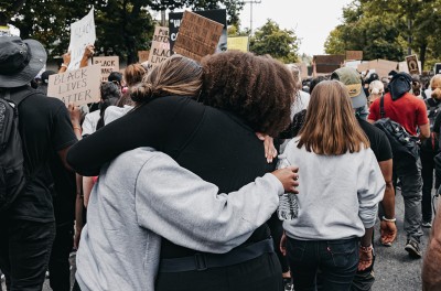 Dos mujeres en medio de una multitud se abrazan a la vez que se manifiestan en pro de la justicia racial, Seattle, EE.UU., 10 de junio de 2020. © Duncan Shaffer/UNSPLASH