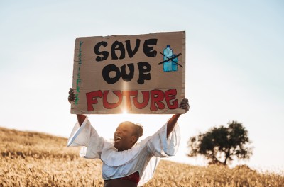一位妇女站在野外，手持标语呼吁提高对气候变化的认识。图片来源：盖蒂图片社/Leo Patrizi