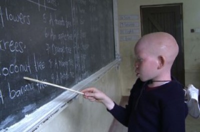 Photo of a child in a classroom pointing at the blackboard