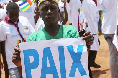 Young man of colour holding sign that reads PAIX (Peace)