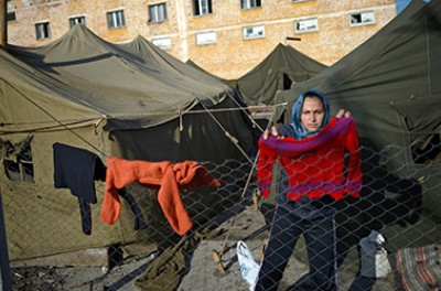 A woman stands behind a fence at a refugee camp