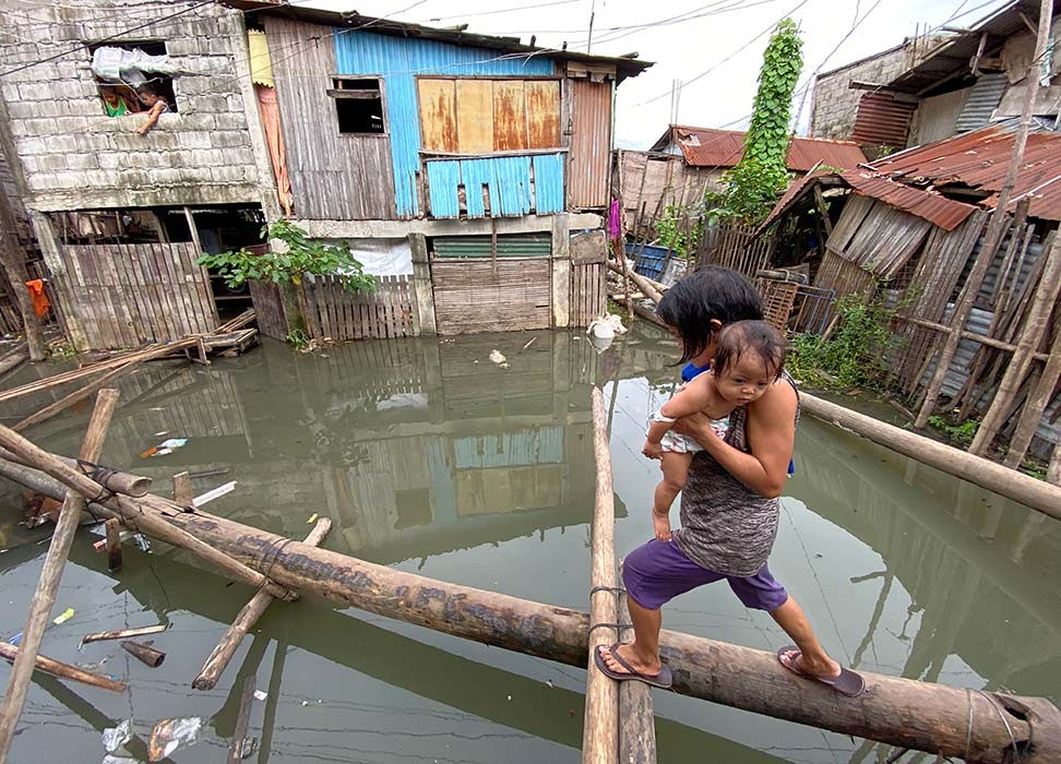 A villager holding a baby maneuvers on a makeshift bridge at a flooded community brought by Typhoon Conson in Muntinlupa city, Metro Manila, Philippines, 10 September 2021 © Francis R. Malasig/EPA-EFE