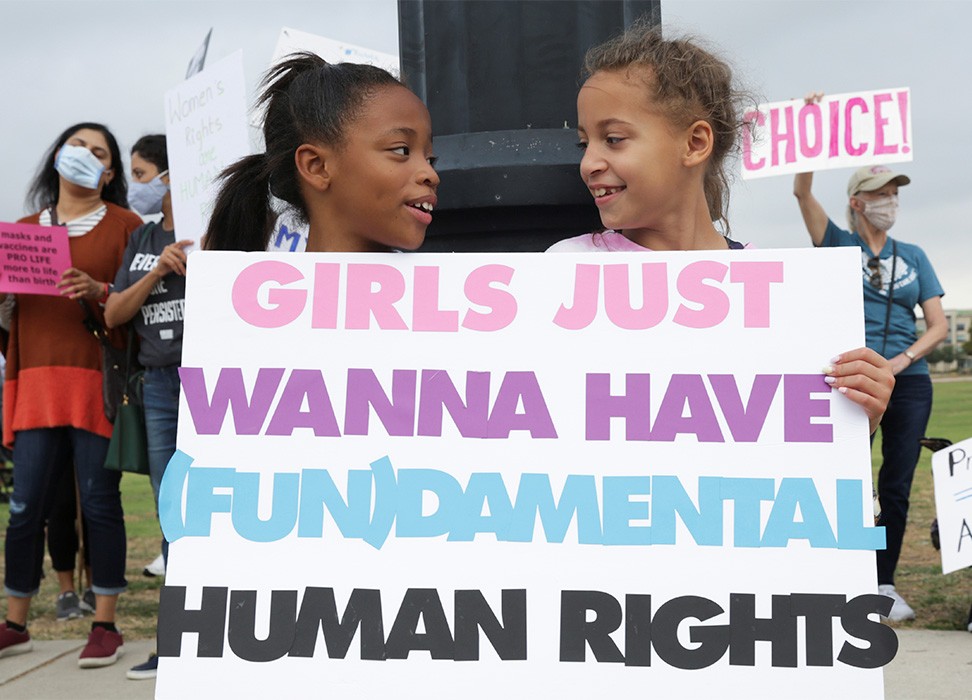 فتاتان تحملان لافتة أثناء مشاركة مناصرات الحقوق الإنجابية في مسيرة المرأة في تكساس. © رويترز/ شلبي توبر