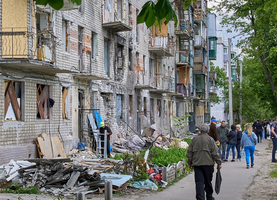 2022年5月25日，乌克兰哈尔科夫郊区，当地人走过一栋在炮击中被毁的住宅楼。©欧新社-埃菲社/SERGEY KOZLOV