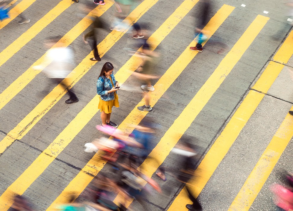在繁忙的人行横道上，一位女士驻足查看手机信息，周围穿梭的人群变成模糊的光影。© 盖帝图像