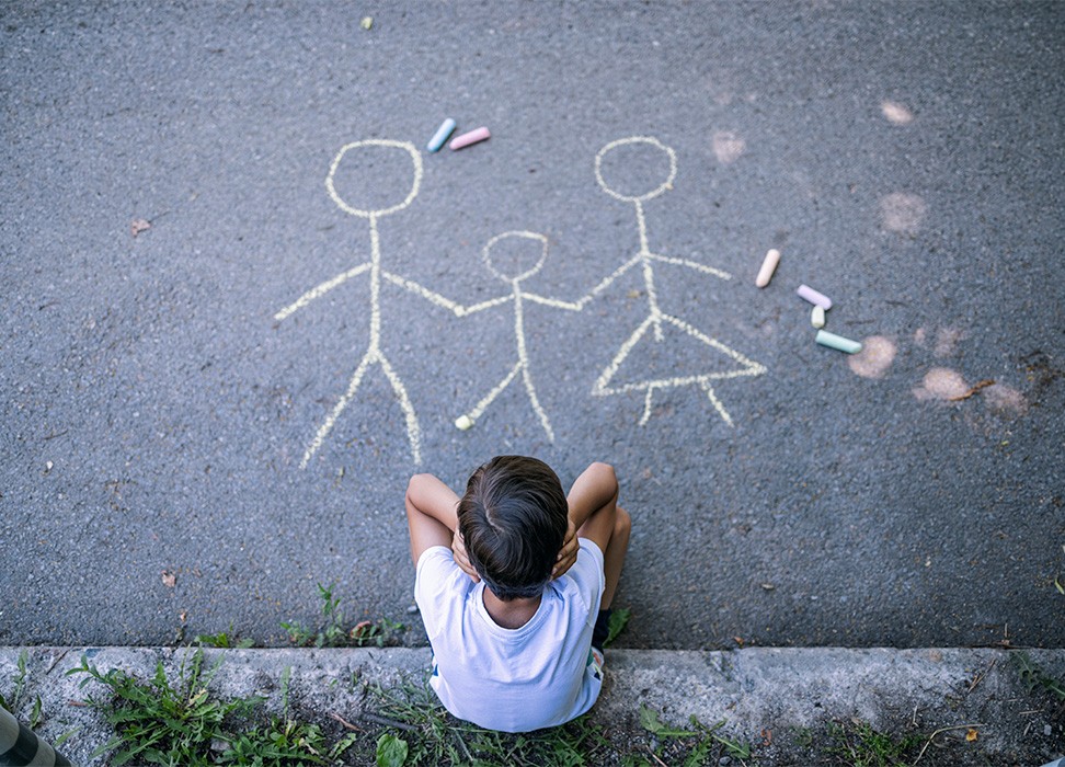 Image en plongée montrant un petit garçon à l’air triste devant un dessin de sa famille. © Getty Images