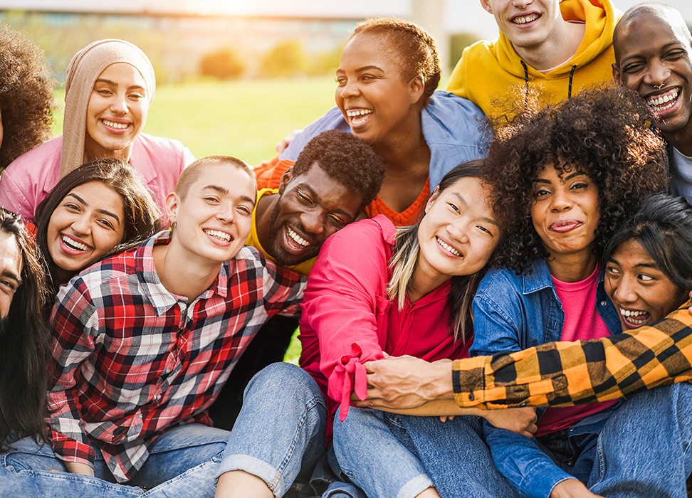 A group of people of diverse ethnicities sit together, hug, and laugh. © Getty Images/DisobeyArt