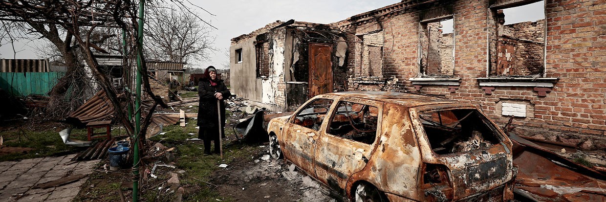 Женщина стоит у своего разрушенного дома и машины в Украине