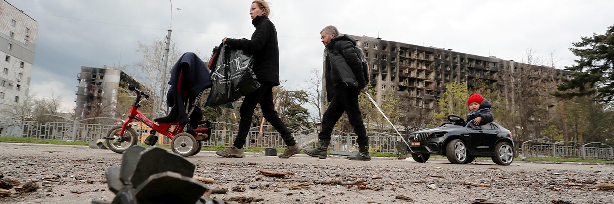 Une famille marche dans la rue près d’un quartier résidentiel détruit durant le conflit qui oppose l’Ukraine à la Fédération de Russie dans la ville portuaire de Marioupol, au sud de l’Ukraine, le 22 avril 2022