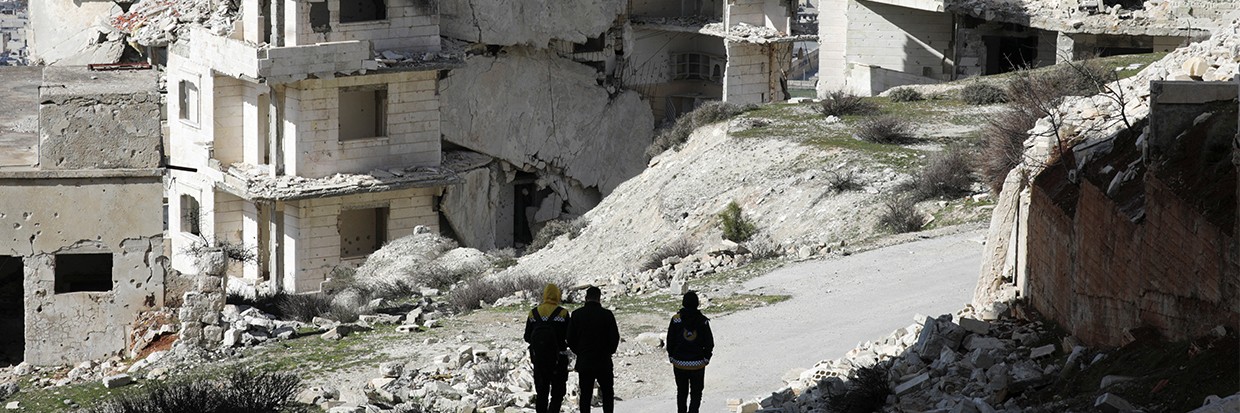 Un grupo de personas pasa por delante de edificios dañados en Jabal al-Arbaeen, en la provincia meridional de Idlib, Siria, el 20 de marzo de 2022. © Reuters