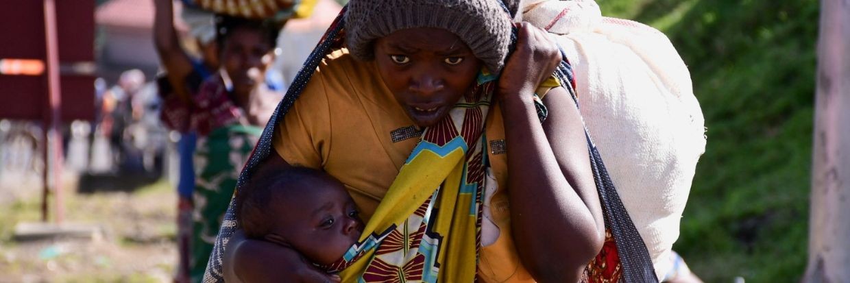 2021年11月10日，乌干达西部的布纳加纳过境点，一名刚果平民在逃离袭击者与刚果民主共和国和乌干达军队之间的新一轮战斗后，背着孩子和物品。