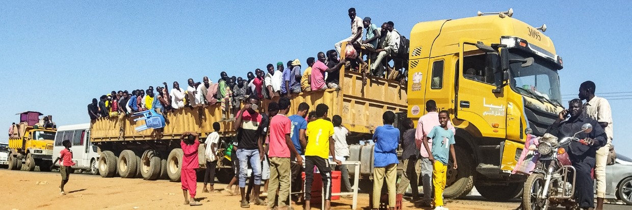 2023年12月16日，因苏丹冲突而流离失所的人们登上了一辆卡车的车斗，这辆卡车行驶在杰济拉州首府瓦德迈达尼的公路上。据法新社记者报道，12月15日，苏丹军方与准军事团体爆发战斗，战火席卷了作为流离失所者援助枢纽的瓦德迈达尼，导致因持续八个月的战争而流离失所的平民不得不再次逃离。© 法新社