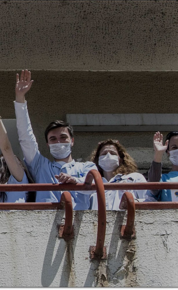 Health care workers in protective face masks wave from a balcony