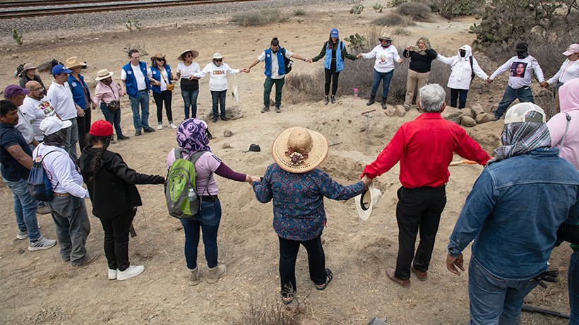 A group of standing people in a circle holding hands. 	