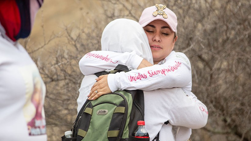 Two women embrace in a field. 