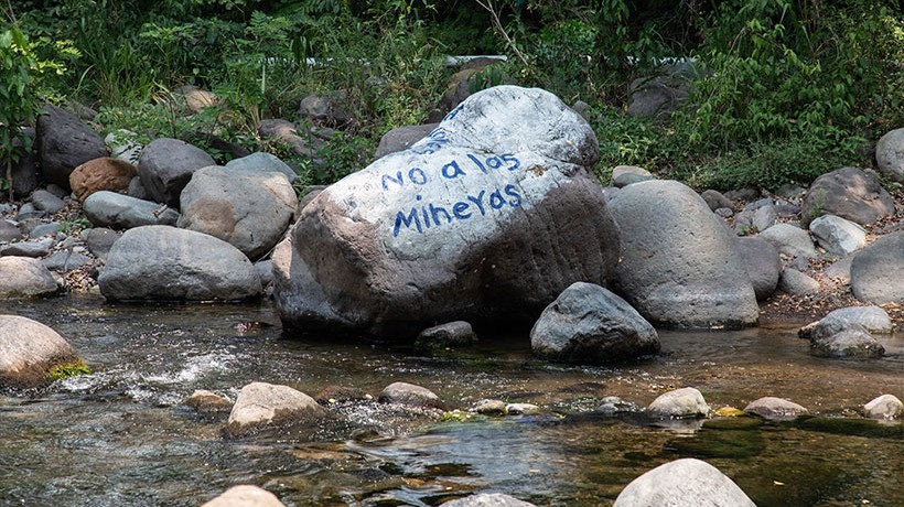 A big stone with something written on it on it near a stream