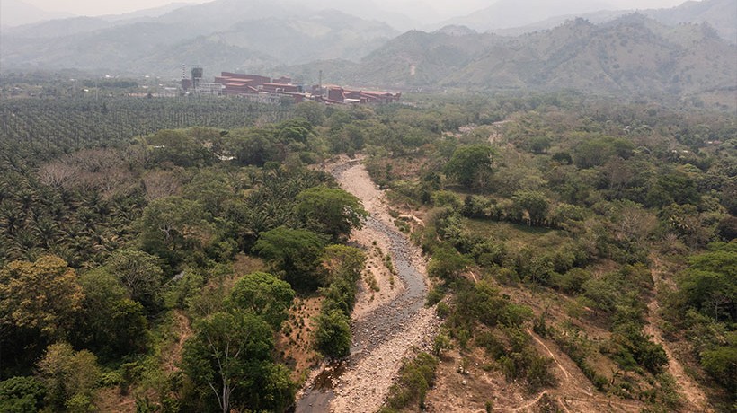 A view of the mountains, a forest, a river, and a red big building on top