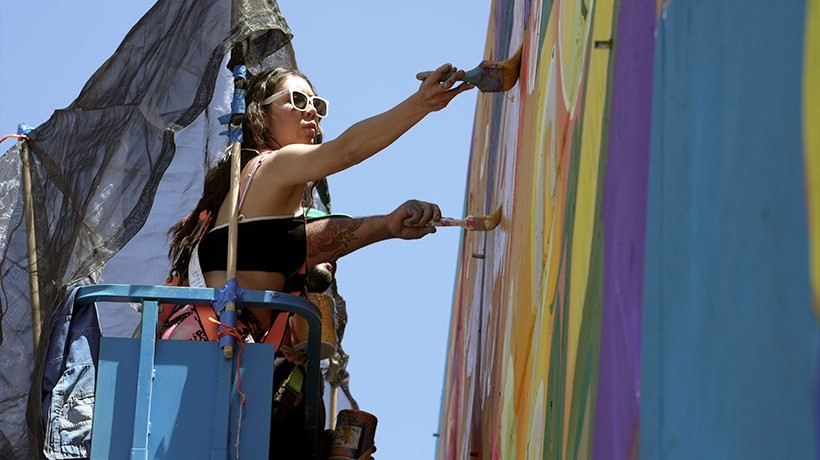 : A human standing in a scaffolding painting a wall.